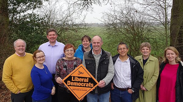 Lib Dem councilors with trees each side of them and a field behind 