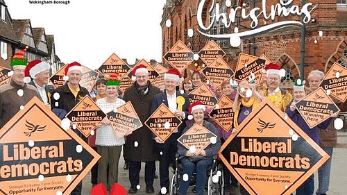 Lib dems by Wokingham town hall with Santa hats etc superimposed on top. The Wokingham Lib Dem logo has been made to look like Santa’s sleigh being pulled by Lib Dem