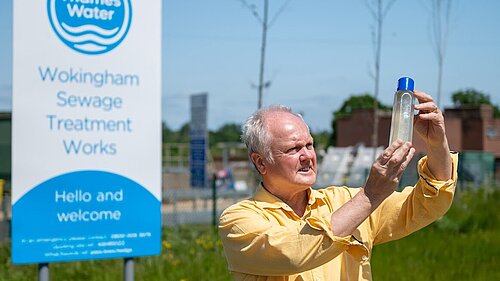 Clive Jones MP stood outside of Thames Water Sewage Treatment Works, inspecting a glass bottle containing polluted river water.