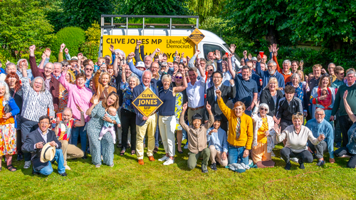Big group of cheering Lib Dems outside on a sunny day, in the background is a van with "Clive Jones MP" and "Thank you Wokingham" on it