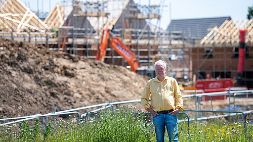 Clive Jones stood in front of a building site. Half-built houses and construction equipment can be seen in the background.